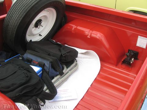 1968 Ford Mustang - The interior of a red pickup truck bed contains a spare tire, various bags, and folded chairs, with a yellow vehicle visible in the backgro…