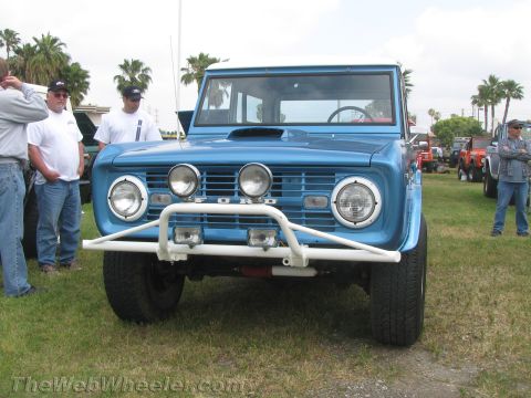 1968 Ford Mustang - A blue Ford Bronco is parked on grass with other vehicles and people nearby.