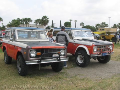 1968 Ford Mustang - Two Ford Broncos are parked on a grassy area, with a building and palm trees in the background.