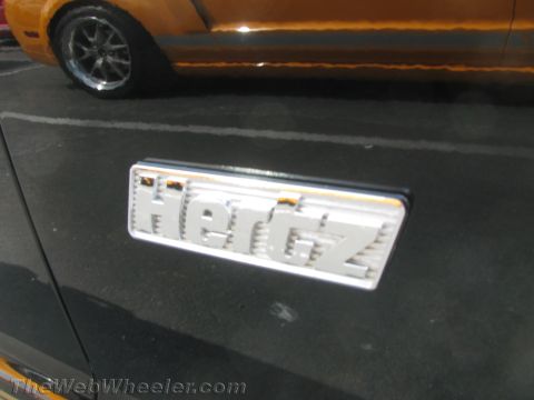 1968 Ford Mustang - A close-up of a Hertz emblem on a car door, with another vehicle partially visible.