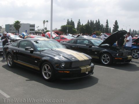 1968 Ford Mustang - Two black Ford Mustangs with gold stripes are parked at an outdoor car show.