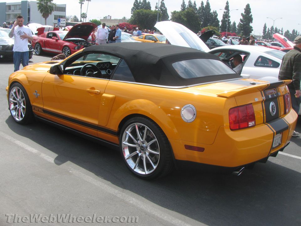 Yellow convertible Mustang with black racing stripes and chrome wheels parked at a car show
