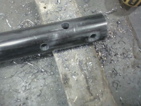 1992 Ford F-350 - A metal pipe with multiple holes drilled into it sits on a wooden surface, surrounded by metal shavings.