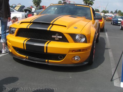 1968 Ford Mustang - A yellow 2008 Ford Mustang Shelby GT500 convertible is parked in a lot, displaying its iconic black racing stripes.