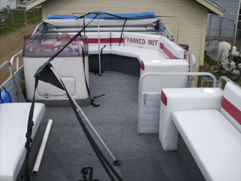 Pontoon boat interior with white seats, a baby in the driver's seat, and a canopy overhead. Text on the seat…
