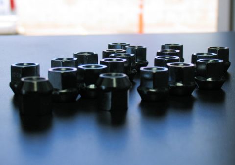 1984 Ford Bronco - A collection of black lug nuts is displayed on a dark, reflective surface, with a watermark for Supermotors.net visible.