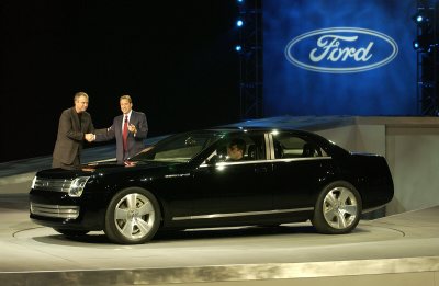 2004 Ford 427 - A black luxury sedan is presented on a stage with a Ford logo in the background.