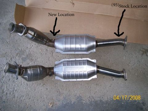 1995 Mercury Grand Marquis - A matched pair of stainless catalytic converter assemblies laid out on a concrete garage floor against a cardboard sheet, each combining a…