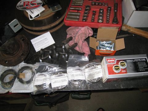 1996 Ford Bronco - Various automotive parts and tools are laid out on a workbench, including wheel bearings and a socket set.