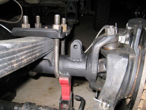1996 Ford Bronco - Under-vehicle close-up of a leaf-sprung front axle showing the leaf pack clamped to the axle tube by U-bolts and a spring plate, with a fre…