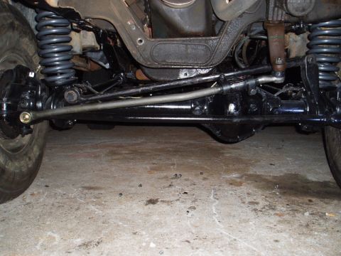 1980 Ford Bronco - The photo shows the front axle, steering linkage, and suspension of a vehicle, likely taken from underneath.
