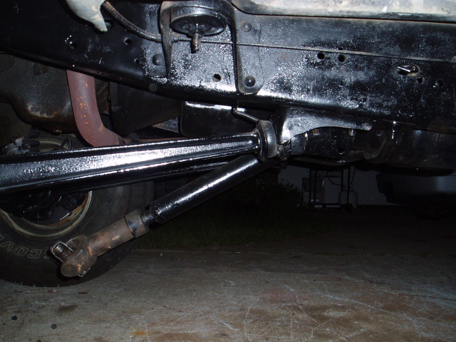 Undercarriage of a vehicle with black painted frame, driveshaft, and exhaust pipe. Tire visible on left