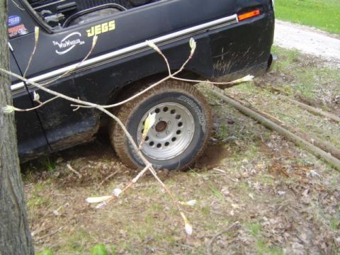 1979 Ford Bronco - Close-up of the rear quarter of a black truck buried to the rim in mud, with a Firestone tire on a silver steel wheel and deep ruts dug int…
