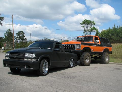 1979 Ford Bronco - A lifted orange Ford Bronco is parked behind a black pickup truck on a cloudy day.