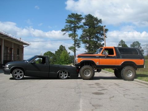 1979 Ford Bronco - A lifted orange 1979 Ford Bronco is parked next to a slammed black pickup truck on a sunny day.