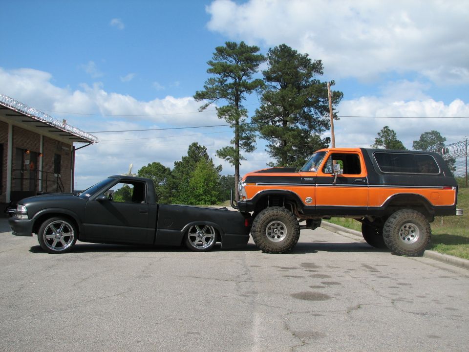 Lifted orange 1979 Ford Bronco next to a lowered black pickup truck