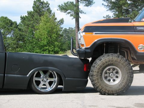 1979 Ford Bronco - An orange 1978 Ford Bronco is parked very close to a black pickup truck.