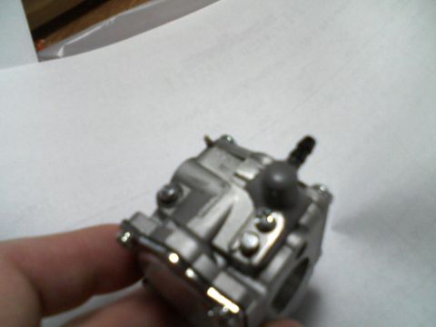 2000 Chevrolet Tahoe - A close-up view of a carburetor, likely for a small engine, is held by a hand against a white background. The Supermotors.net logo is visib…