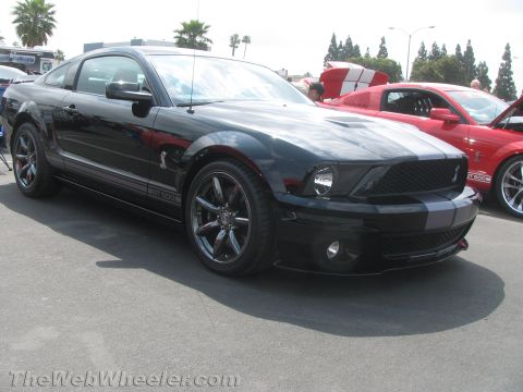 1968 Ford Mustang - A black Ford Mustang Shelby GT500 is parked next to a red Mustang, both with racing stripes.