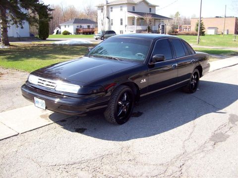 1996 Ford Crown Victoria - A black sedan with tinted windows and custom rims sits on a driveway.