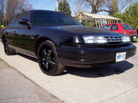 1996 Ford Crown Victoria - Black Ford Crown Victoria with aftermarket wheels and a red car in the background.
