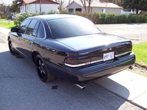 1996 Ford Crown Victoria - This black Ford Crown Victoria has tinted windows and aftermarket rims, parked curbside in front of houses.