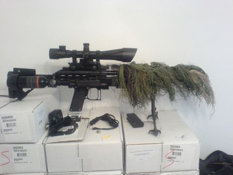 1985 Ford Bronco - A sniper rifle equipped with a scope, camouflage netting, and a CO2 tank is displayed on top of boxes.
