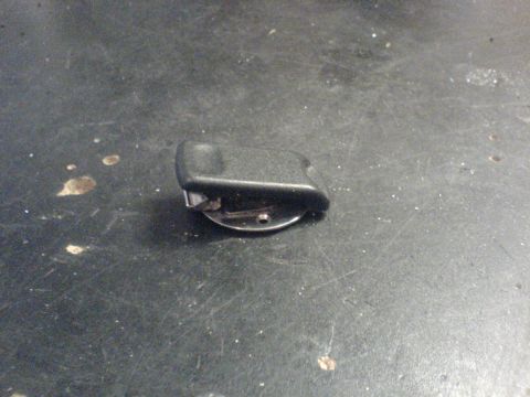 1985 Ford Bronco - A black plastic part with a metal clip is shown on a dark surface.