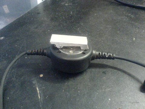 1985 Ford Bronco - A small metal component is attached to a black circular device with cables, resting on a textured surface.