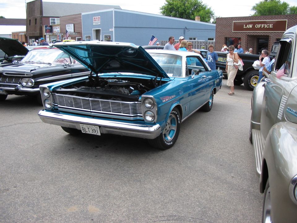 Teal 1965 Ford Galaxie hardtop with hood open showing engine at an outdoor car show