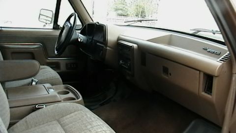 1990 Ford Bronco - The interior of a truck features a tan dashboard, steering wheel, and cloth seats with a center console.
