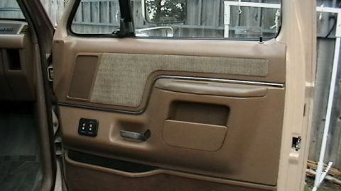 1990 Ford Bronco - Interior door panel detail of a truck, possibly from the 1990s, a two-tone fabric insert and a pull handle.