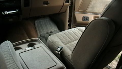 1990 Ford Bronco - The interior of a vehicle features patterned cloth seats, a center console with cup holders, and floor mats.