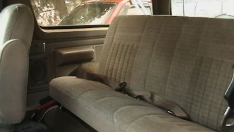 1990 Ford Bronco - Rear interior of a 1990 Ford Bronco, showing the bench seat and door panel. Another vehicle is visible through the window.