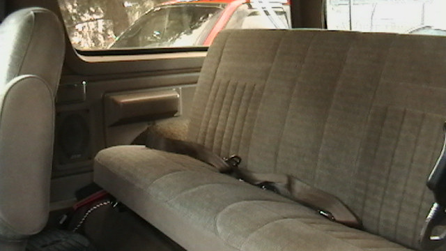 Tan cloth bench seat interior of a truck with seatbelt and door panel speaker visible