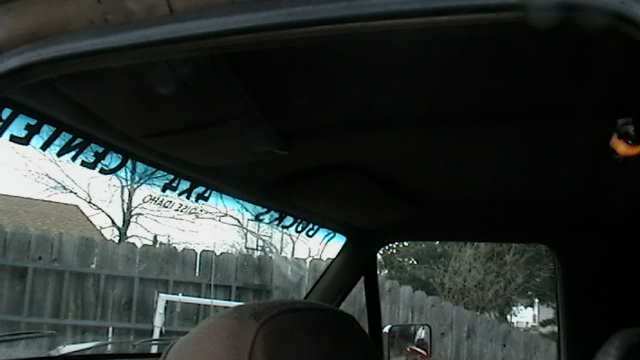 View through windshield of a vehicle interior, showing a sun visor and a sticker on the windshield