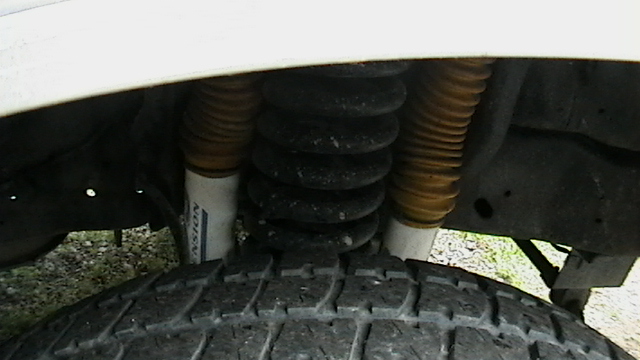 Close-up of coil spring and twin shocks with yellow boots above a tire under a white fender