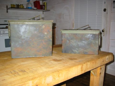 1996 Ford Bronco - Two metal ammo cans with a camouflage pattern sit on a wooden workbench in front of shelves.