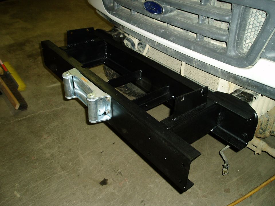 Black metal bumper assembly with a winch, attached to a white Ford truck's front grille