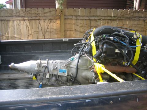 1996 Ford Crown Victoria - A vehicle engine and transmission assembly is loaded into the bed of a truck, secured by yellow straps.