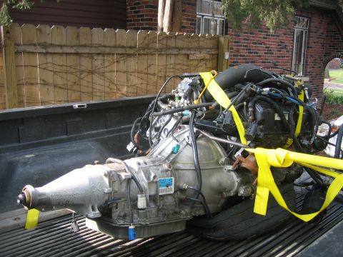1996 Ford Crown Victoria - Engine and transmission assembly, likely removed from a vehicle, is being transported in the bed of a pickup truck.