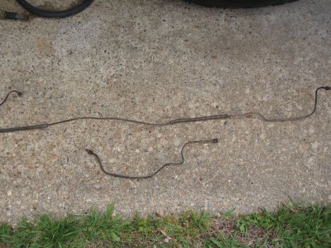 1968 Shelby GT500 - Two metal brake lines are shown on a concrete surface with grass in the foreground.