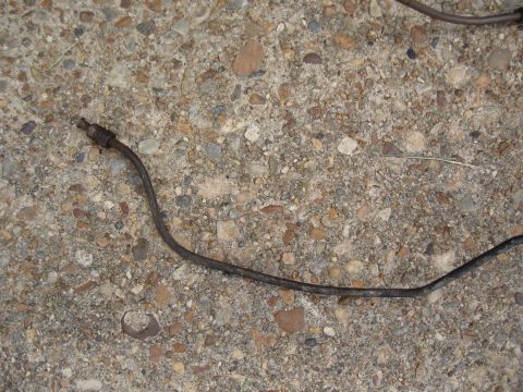 1968 Shelby GT500 - A single, aged brake line lies on a textured concrete ground, showing signs of wear and corrosion.