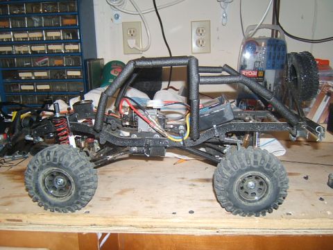 1988 Ford Bronco - Side view of an RC crawler chassis a prominent roll cage and exposed electronic components.
