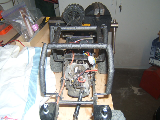 RC crawler chassis with exposed motor, suspension, and wiring, held in a vise