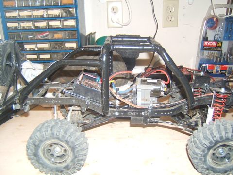 1988 Ford Bronco - Side view of an RC crawler chassis with exposed components and a roll cage.