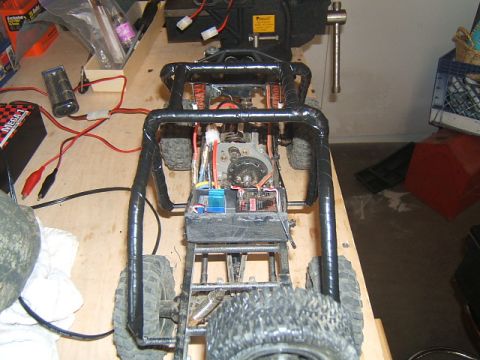 1988 Ford Bronco - The internal components of a radio-controlled buggy are visible, including the motor, battery, and wiring, on a cluttered workbench.