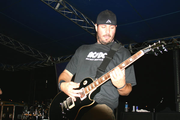 Man in AC/DC shirt playing black electric guitar on stage