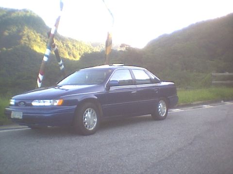 1995 Ford Taurus - A blue sedan is parked on the side of a road with mountains in the background.