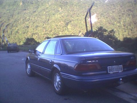 1995 Ford Taurus - This 1995 Ford Taurus is seen from the rear, parked on a street with a wooded hillside in the background.